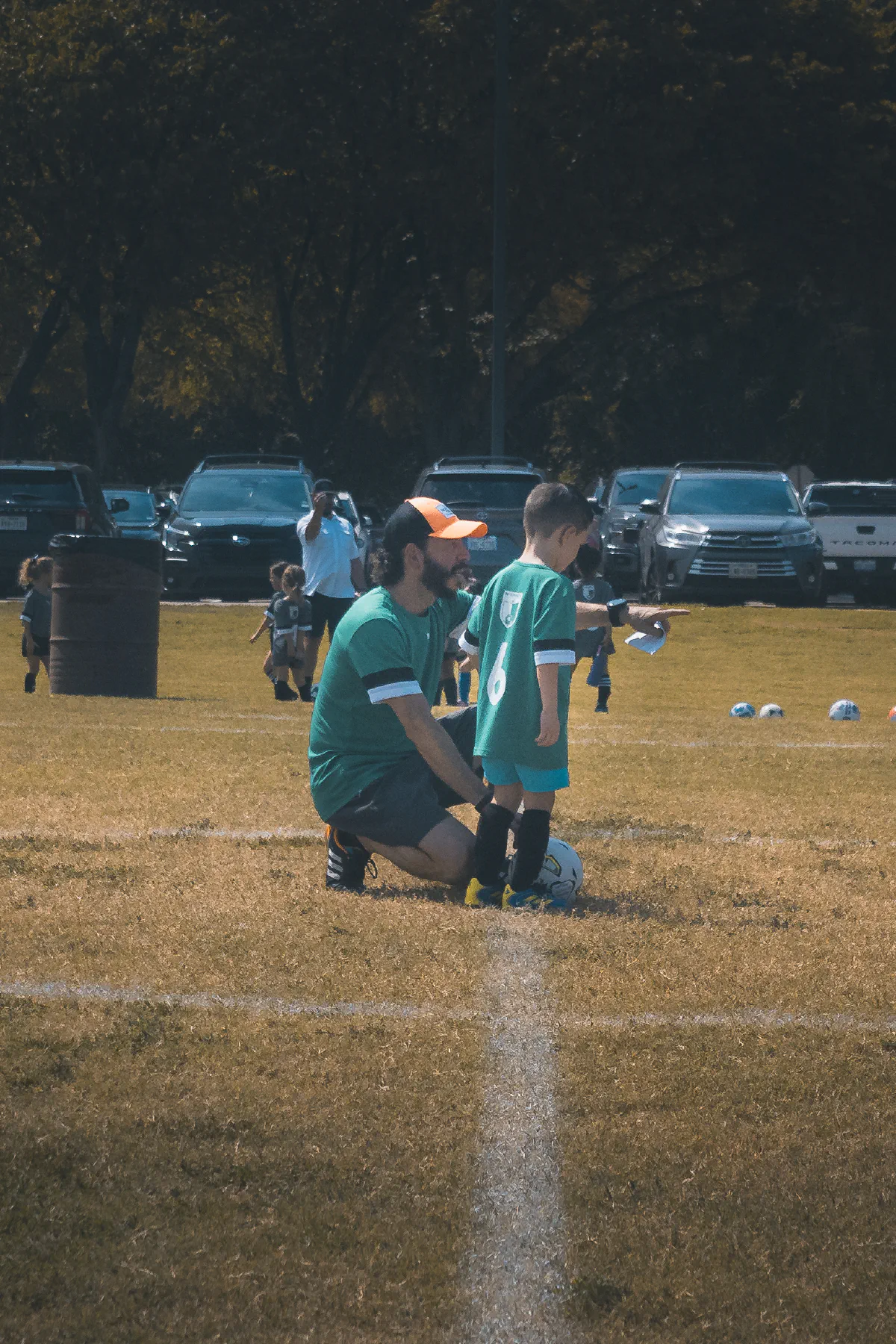 A coach kneels beside a player wearing number 6 and points down the field